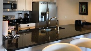 Una cocina moderna con gabinetes blancos, electrodomésticos de acero inoxidable, encimera negra e iluminación colgante.
