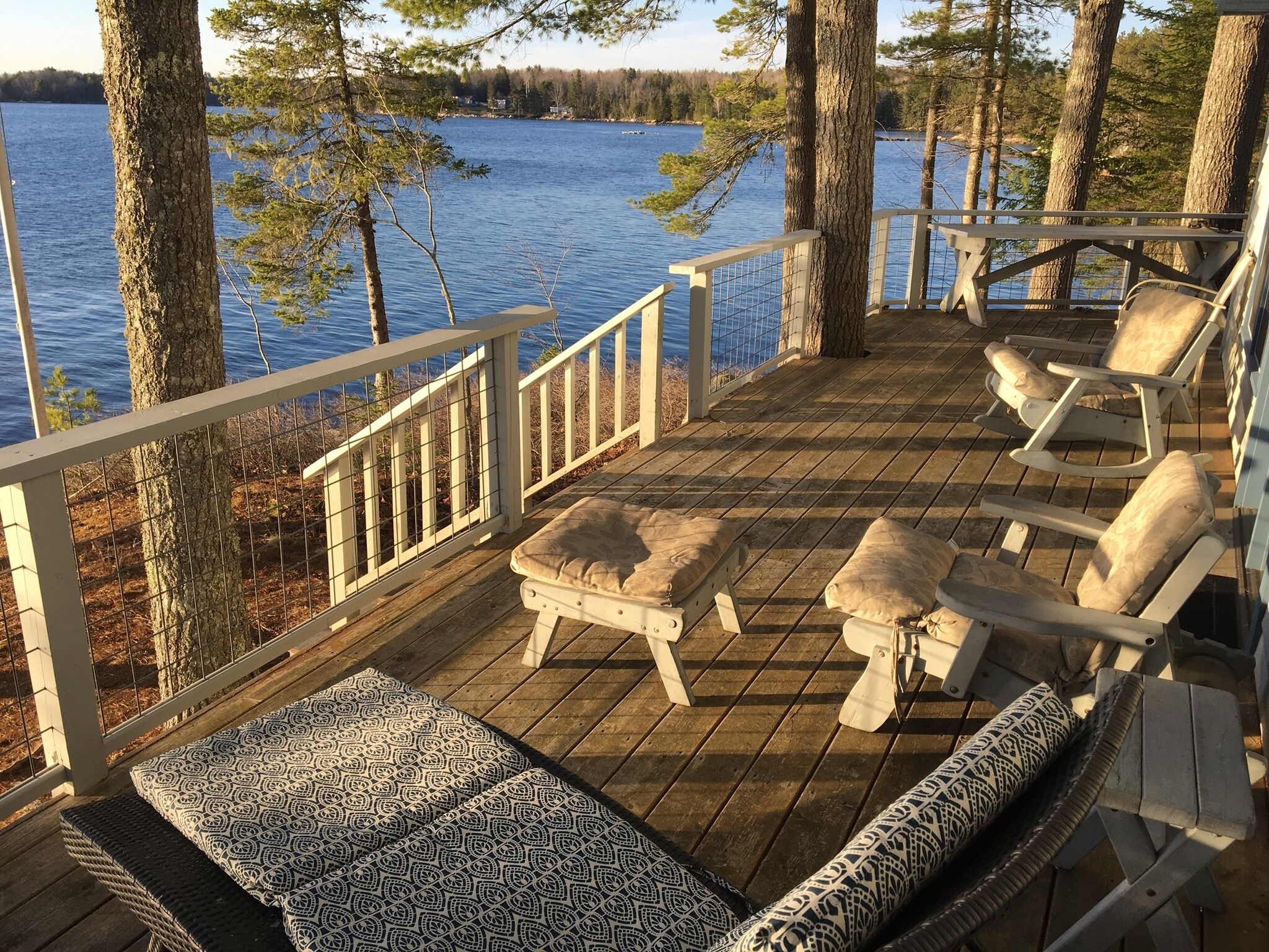 A wooden deck with a railing, two rocking chairs, and a bench with patterned cushions.