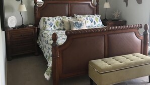 Une chambre à coucher avec un lit en bois, une table de chevet, un banc et des œuvres d’art décoratives au mur.