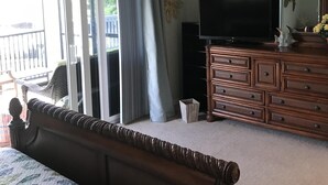 Une chambre à coucher comprenant un lit, une commode, un téléviseur et un ventilateur de plafond.