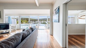 Een ruime woonkamer met een grote grijze bank, een flatscreen televisie op een houten dressoir, en uitzicht op een jachthaven door glazen deuren.