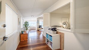 Een gang met houten vloer, een witte deur met sleutelgat, een plant, een bank en een mandje op een plank.