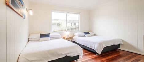 A bedroom with two beds, a window, a nightstand, and a wall-mounted lamp.