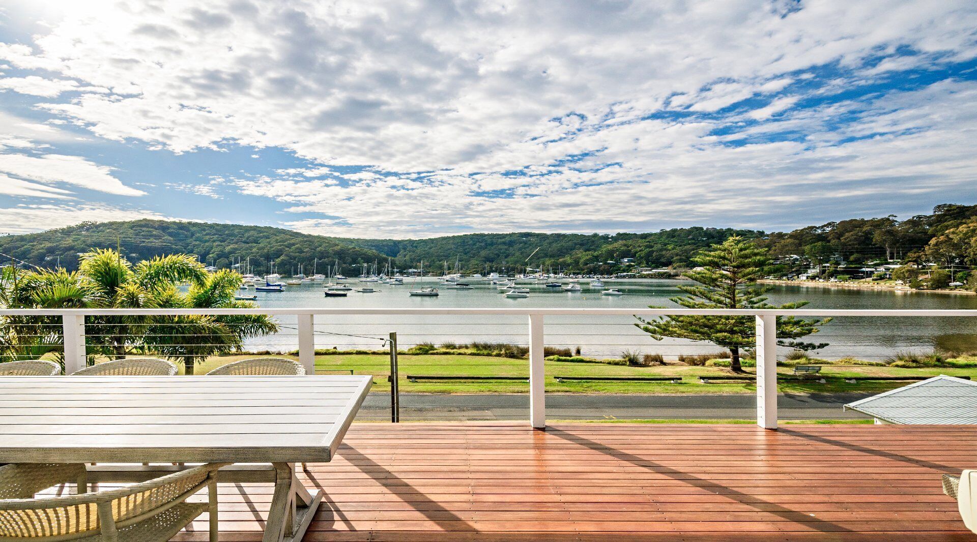 A wooden deck with a table and chairs overlooking a marina with boats.