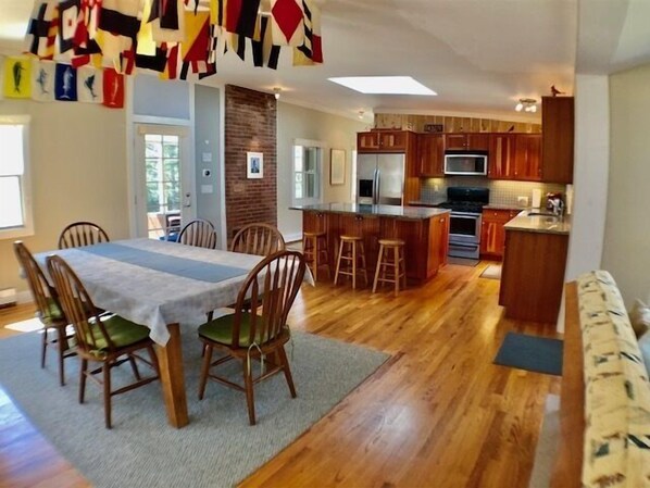 A spacious kitchen with wooden cabinets, a central island with stools, and a dining area with a table and chairs. - Quiet Neighborhood .2 miles to Skaket Beach (1193) (Orleans)