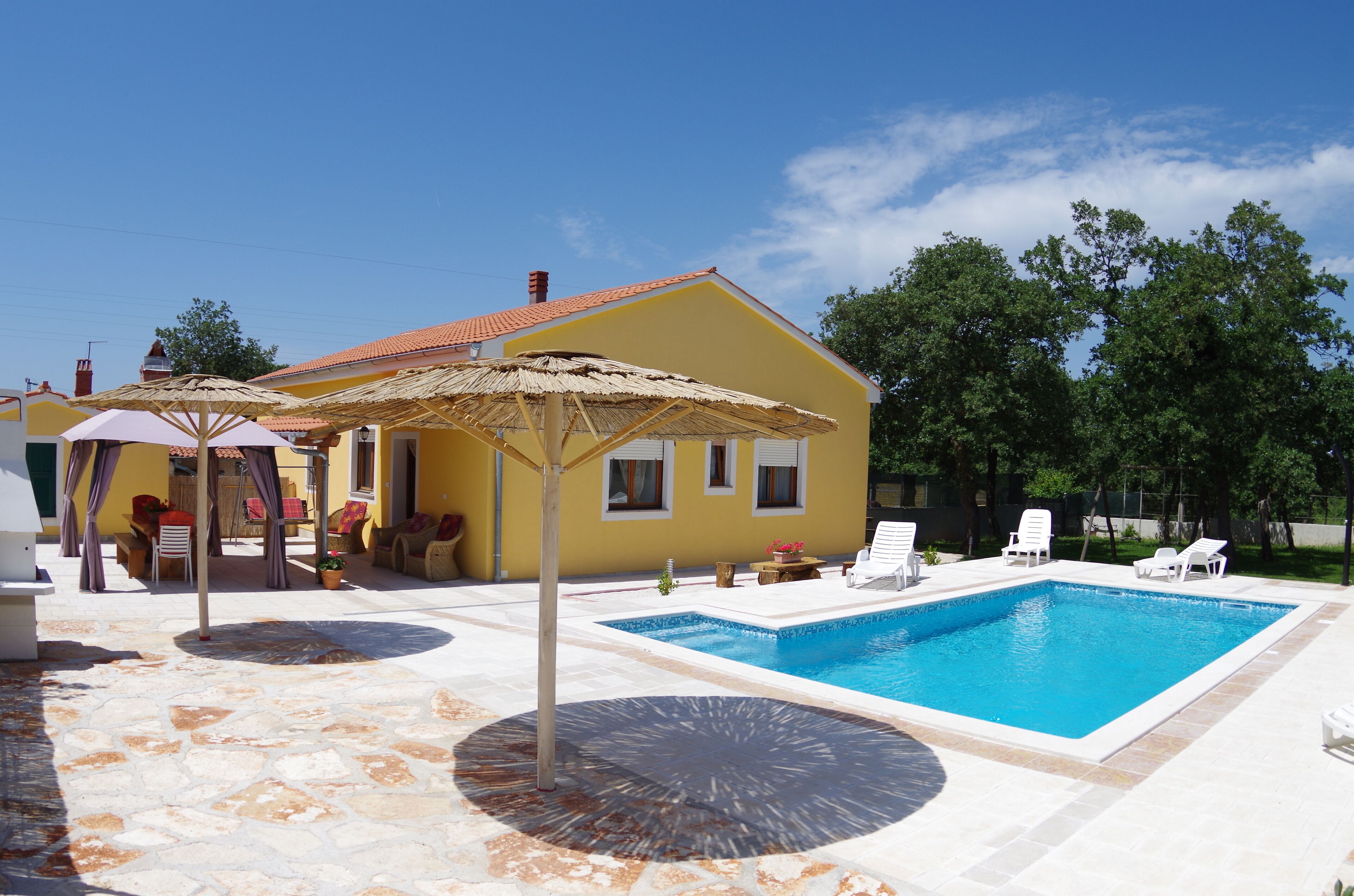 A yellow house with a swimming pool, outdoor furniture, and a pergola.