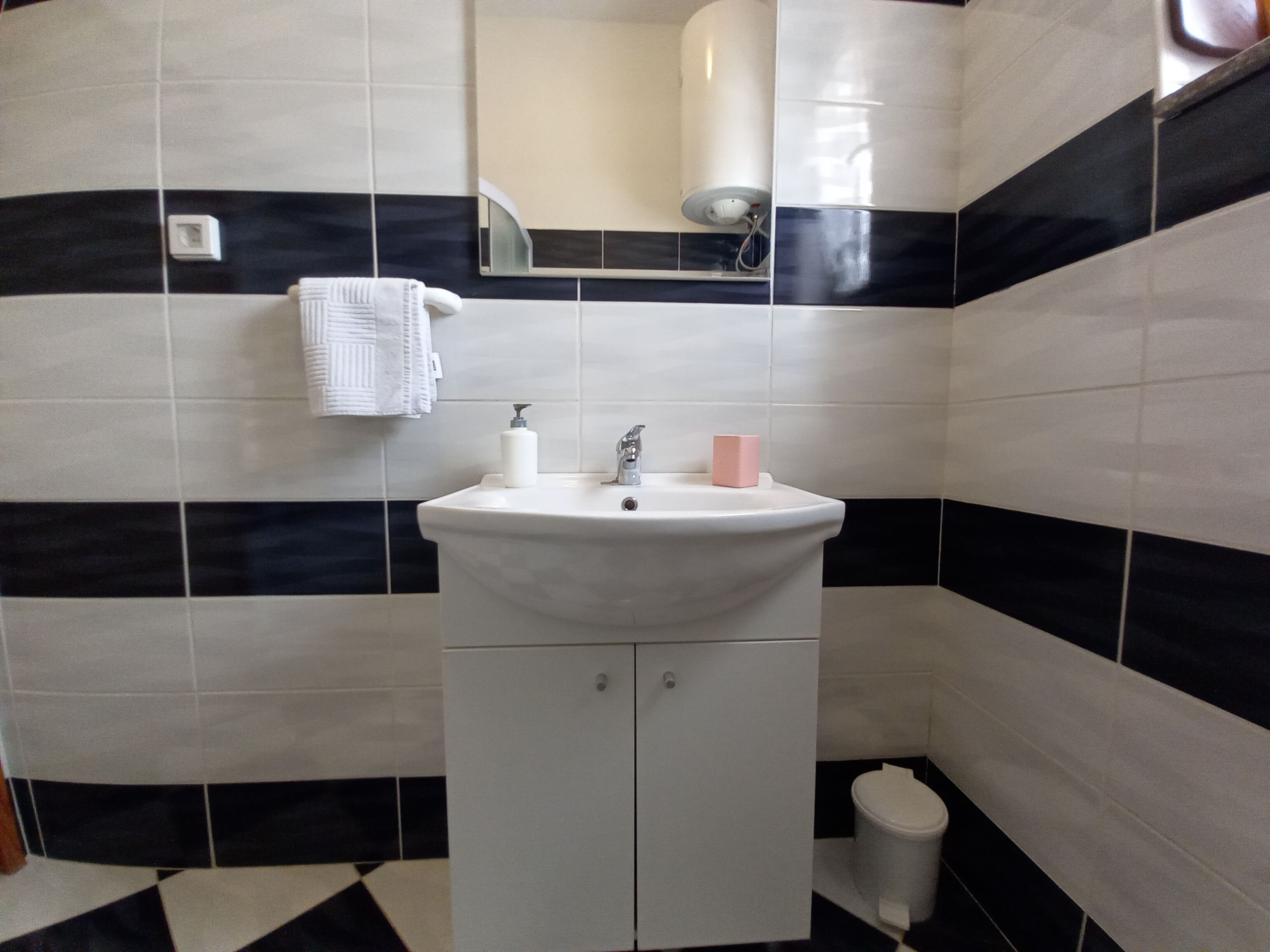 Un bagno con un lavandino bianco, uno specchio, un asciugamano, un dispenser di sapone e un water.