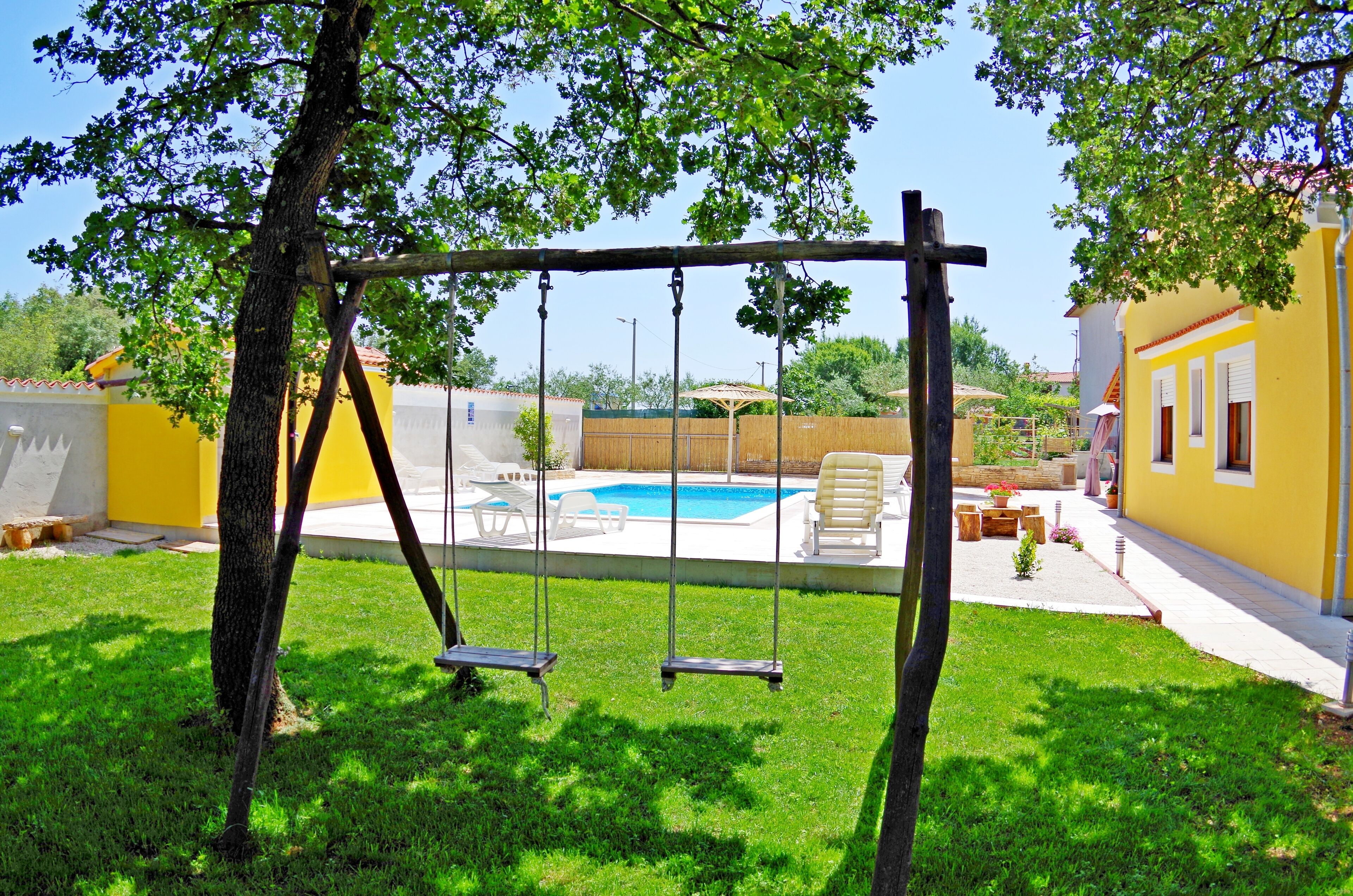 Ein Garten mit Schaukel, Schwimmbecken und einem gelben Haus.