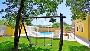 Um quintal com balanço, piscina e uma casa amarela.