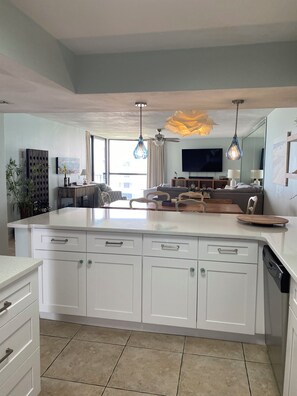 Una cocina moderna con una isla grande, muebles blancos e iluminación colgante.