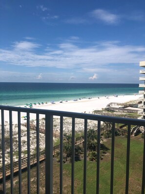 A beach view from a balcony with a clear sky, sandy beach, and a few umbrellas.