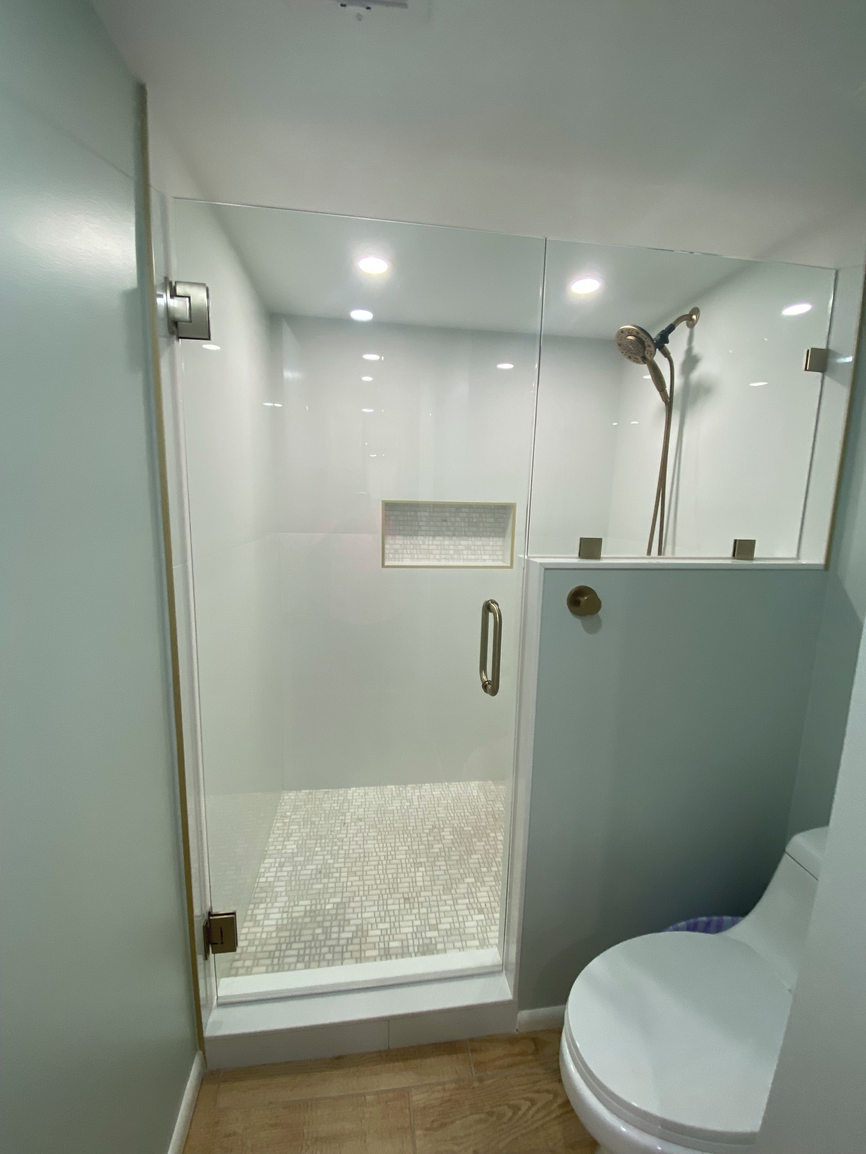 A modern bathroom with a glass-enclosed shower, a toilet, and a mirror above the sink.