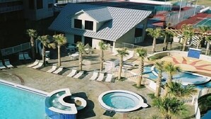 Ein Resort mit Poolbereich, Palmen und einem Gebäude mit Satteldach.