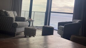 Ein großzügiger Wohnbereich mit großem Fenster zum Meer, einem Deckenventilator und einem Holztisch.