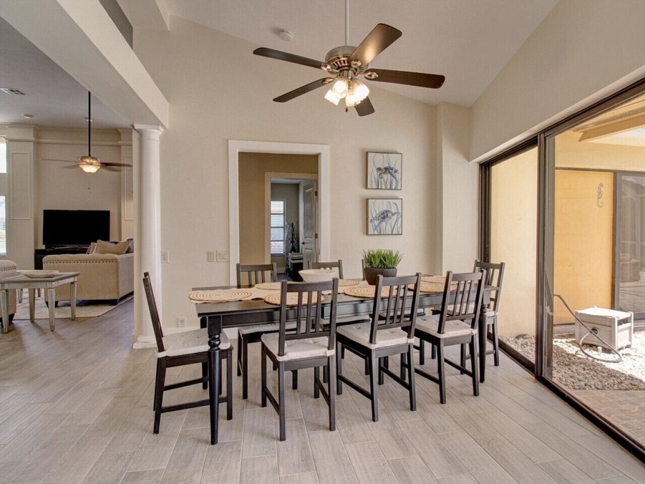 Un espace repas comprenant une grande table et des chaises, un ventilateur de plafond et une vue à travers une porte vitrée.