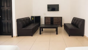 A living room with two dark sofas, a coffee table, a TV on the wall, and a cabinet.