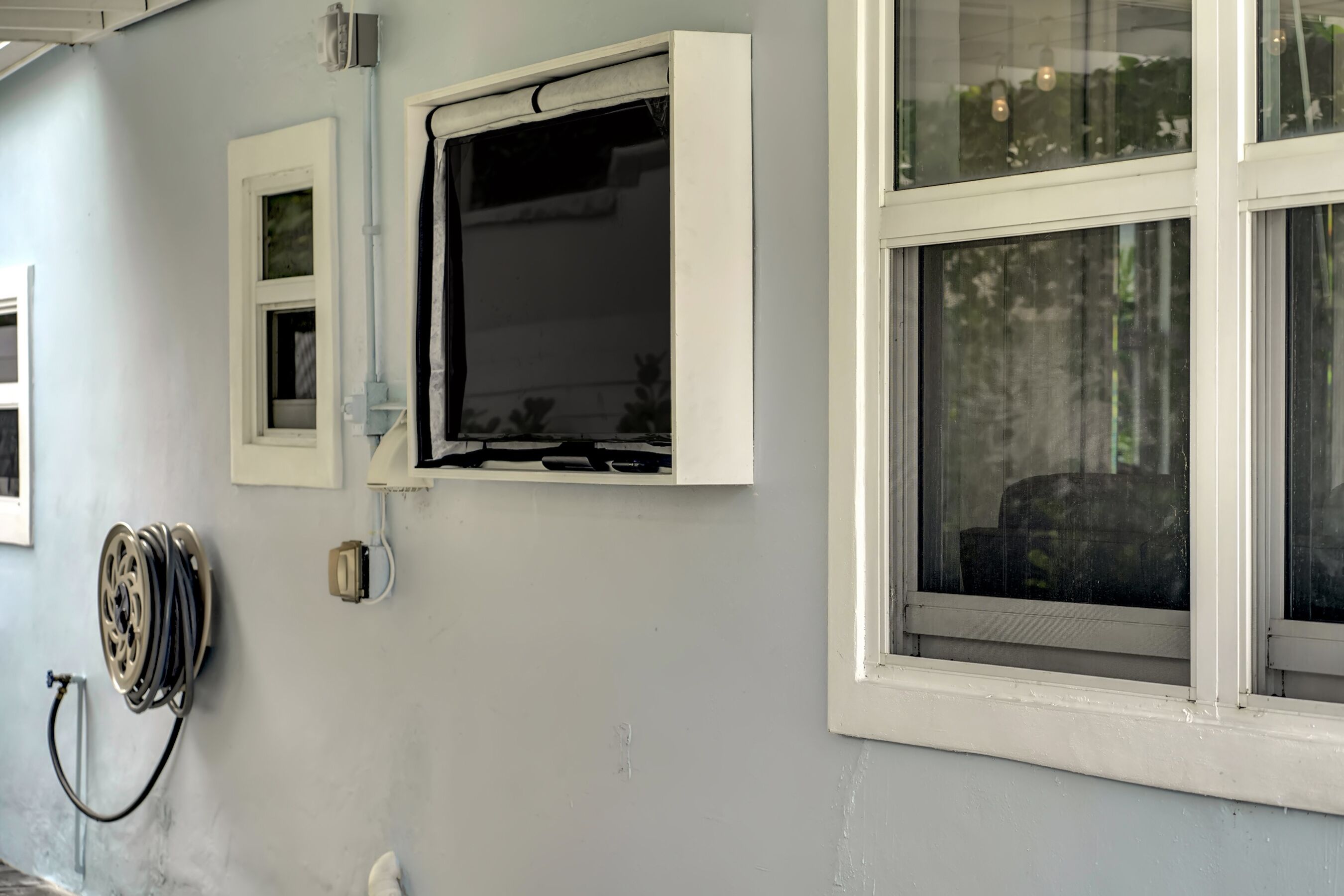 A room with a window, a hose reel, and a wall-mounted electrical outlet.