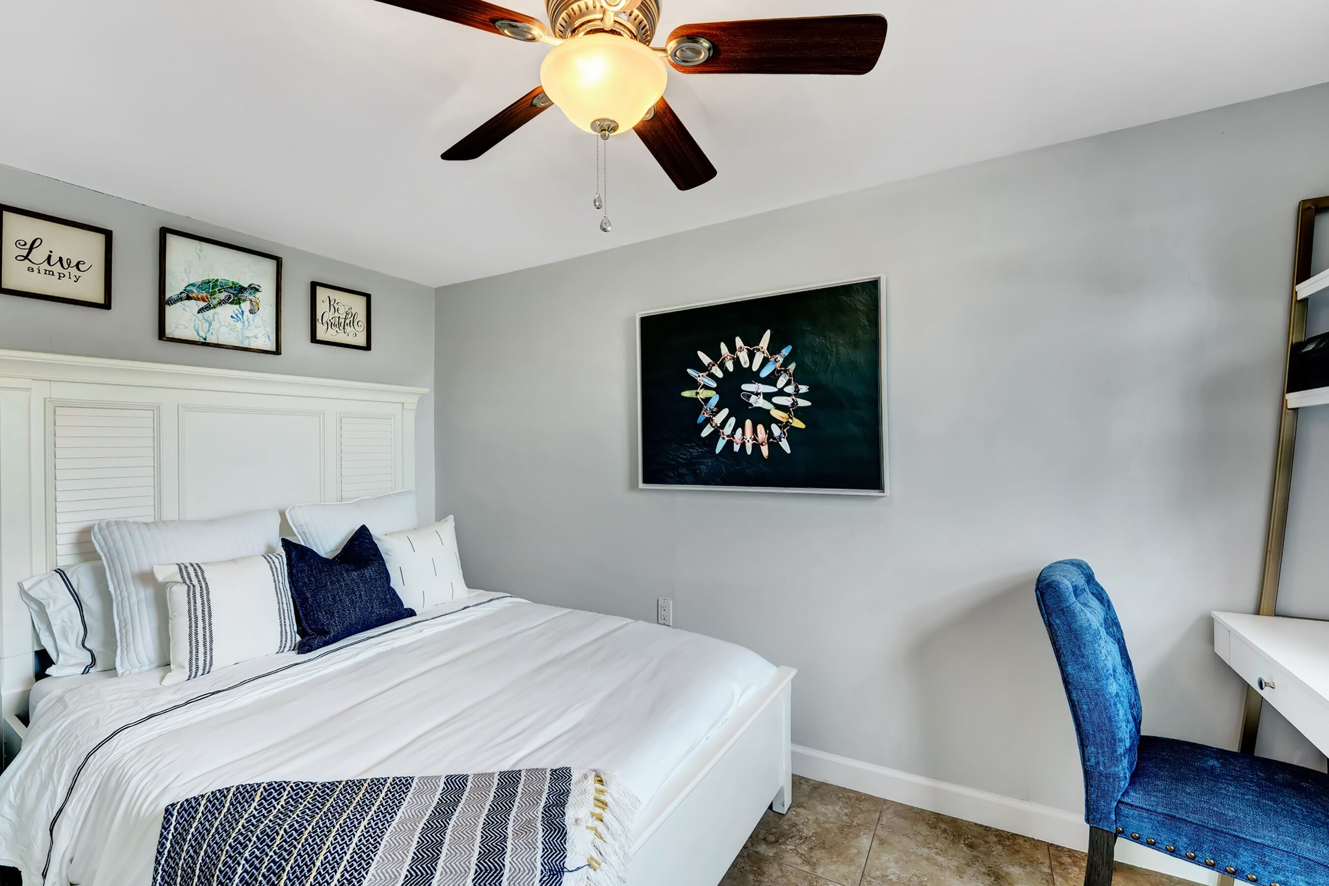 Une chambre à coucher comprenant un lit, un bureau, une chaise, un ventilateur de plafond et des œuvres d’art murales.
