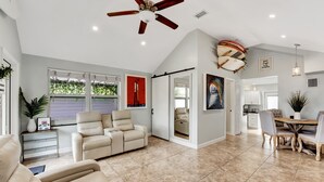 A spacious living room with a beige sofa, a recliner, and a dining area with a wooden table and chairs. - Beach House East of A1A, Private Hot Tub, Outdoor Oasis (Boynton Beach)