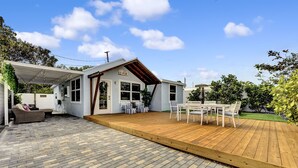 A patio with a wooden deck, a covered seating area, and a white building with a sloped roof. - Beach House East of A1A, Private Hot Tub, Outdoor Oasis (Boynton Beach)