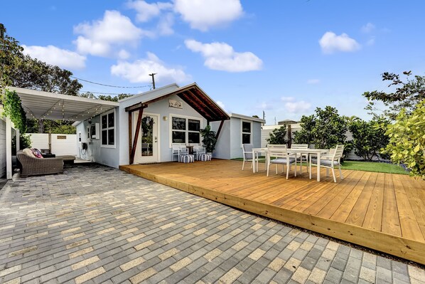 Une terrasse avec une plateforme en bois, un espace salon couvert et un bâtiment blanc doté d’un toit en pente.