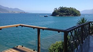 A wooden deck overlooking a calm sea with boats, a small island with dense greenery, and distant mountains. - The most beautiful view in Ilhabela (IlhaBela)