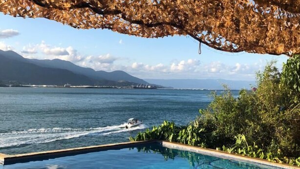 An infinity pool with a wooden deck, a view of the sea, and a boat in the distance. - The most beautiful view in Ilhabela (IlhaBela)