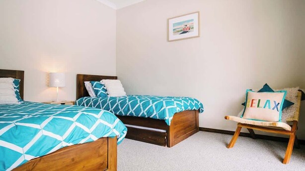 Ein Schlafzimmer mit zwei Holzbett, einem Sessel mit Kissen, einer Lampe und einem gerahmten Bild an der Wand.