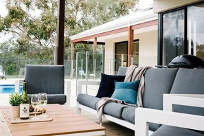 A modern outdoor seating area with a sofa, a wooden table, and a bottle of wine.