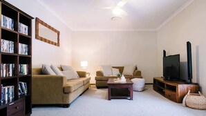 Ein Wohnzimmer mit Bücherregal, zwei Sofas, einem Couchtisch, einem Fernseher und einem Deckenventilator.