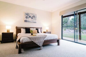 A bedroom with a large bed, two bedside tables, a painting on the wall, and a view through a sliding glass door.