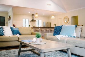 A modern living room with a sofa set, a coffee table, and a kitchen area in the background. - Blue Wren—Chic & Spacious Country Pool House (Margaret River)