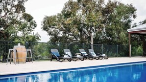 Ein Schwimmbecken mit Liegestühlen und einer überdachten Liegefläche.