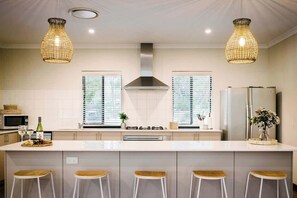 Une cuisine moderne dotée d’un îlot central, de tabourets de bar, de luminaires suspendus et d’une hotte de cuisine en acier inoxydable.