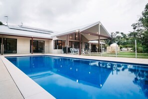 A swimming pool with a covered patio area, adjacent to a building with large windows and a flat roof. - Blue Wren—Chic & Spacious Country Pool House (Margaret River)