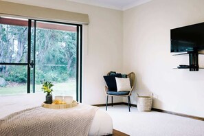 A bedroom with a bed, a chair, a television, and a window with a view of trees.