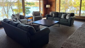 Een knus cabin interieur met een groot raam met uitzicht op een meer, ingericht met een bank, fauteuils en een bijzettafeltje.