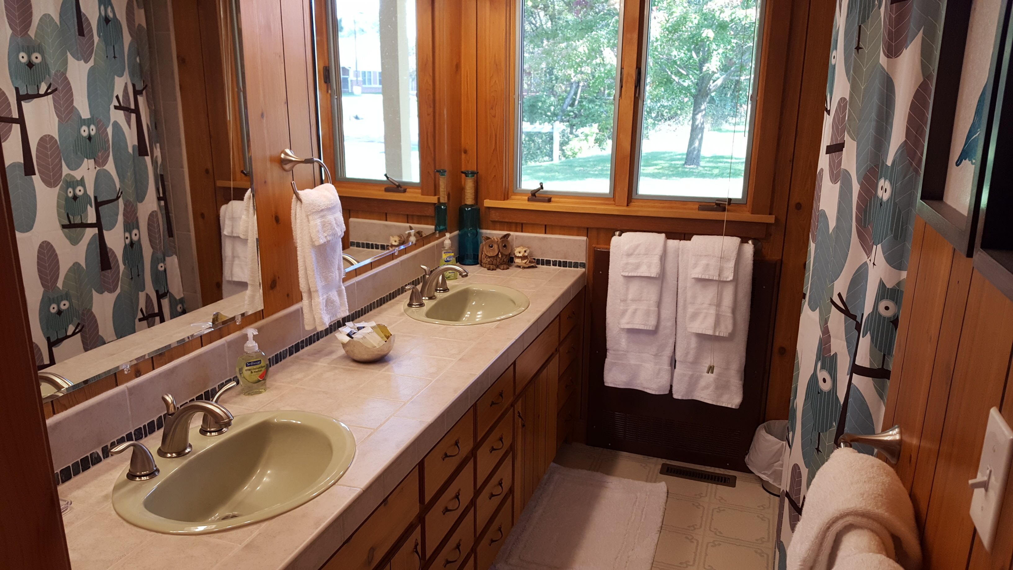 A bathroom with two sinks, wooden cabinets, a mirror, and a window with a view of trees.