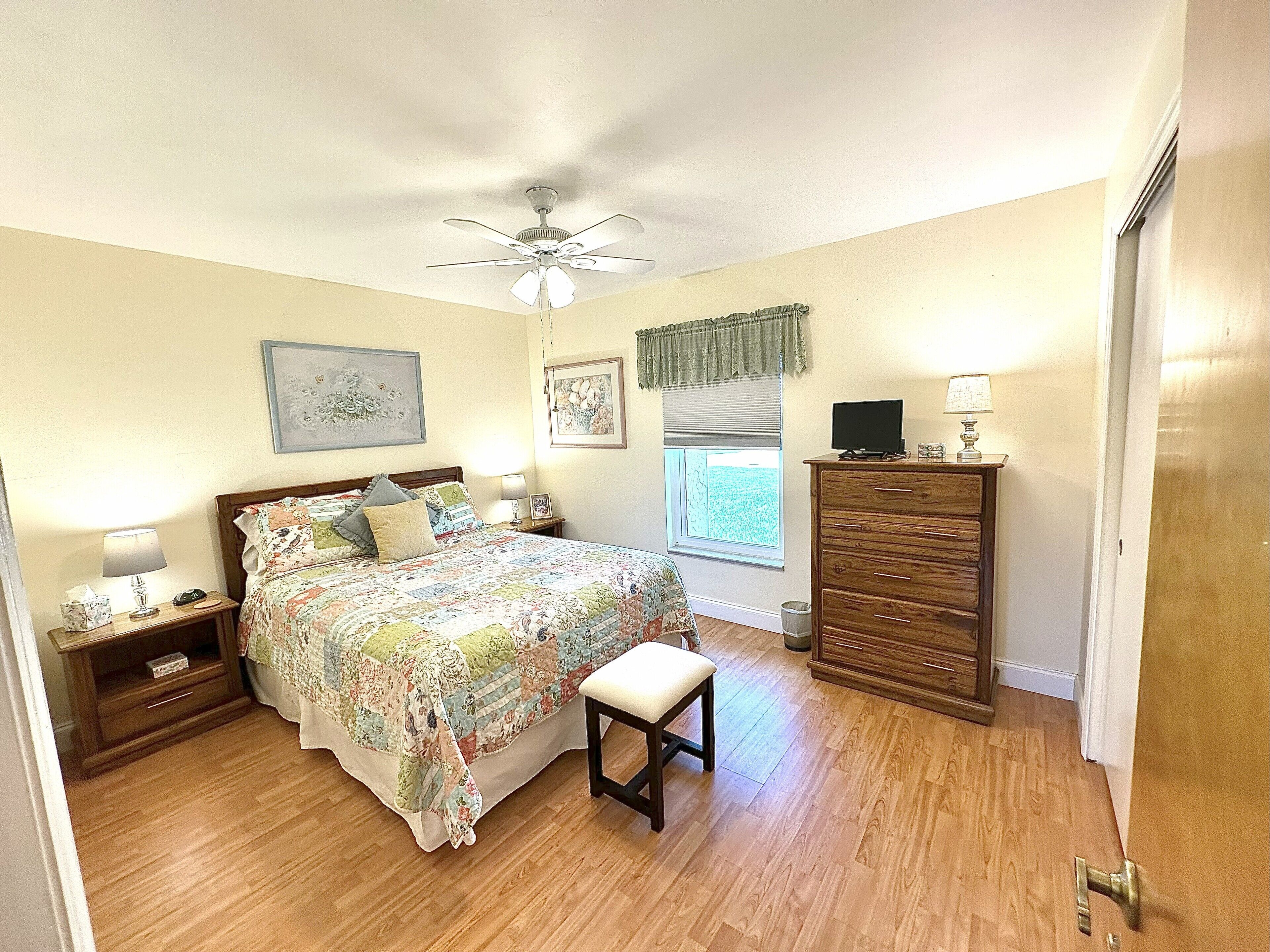 A bedroom with a bed, a nightstand, a dresser, a window with blinds, and a ceiling fan.