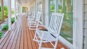 A covered porch with white rocking chairs and a wooden deck.