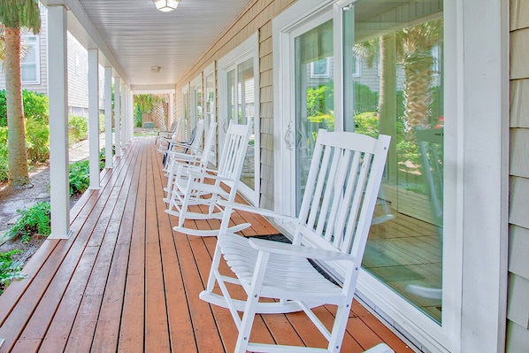 A covered porch with white rocking chairs and a wooden deck.