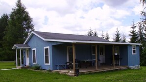 Ein einstöckiges, blaues Haus mit Veranda, einer kleinen angeschlossenen Garage und einem Rasengrundstück.
