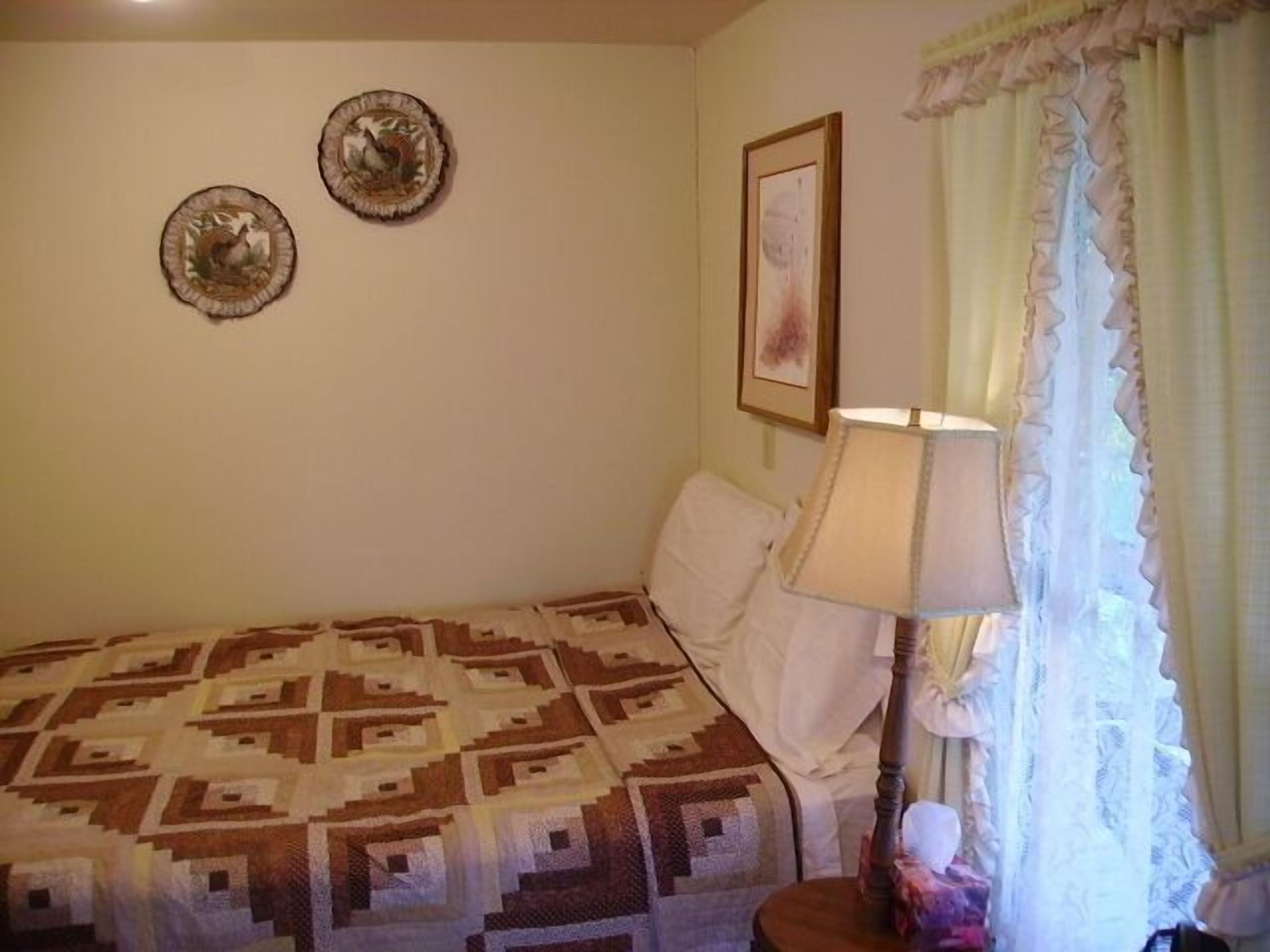 A bedroom with a patterned bedspread, a bedside lamp, and two wall-mounted decorative plates.