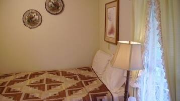 A bedroom with a patterned bedspread, a bedside lamp, and two wall-mounted decorative plates.