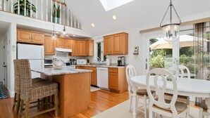 A modern kitchen with wooden cabinets, a central island, and a dining area with white chairs. - Unique Oyster Pond 3bd-2ba home in private setting close to downtown. (Chatham)