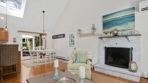 A spacious living room with a fireplace, a dining area, and a view of the outdoors. - Unique Oyster Pond 3bd-2ba home in private setting close to downtown. (Chatham)
