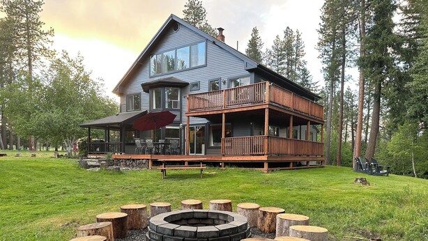 A two-story house with a deck, a fire pit, and a stone fireplace.