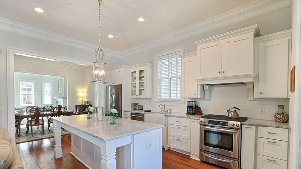 A spacious kitchen with white cabinetry, a central island, stainless steel appliances, and a dining area with a wooden table and chairs. - Heated Pool Access | 5*Clean | Flex Cancelation (Savannah)