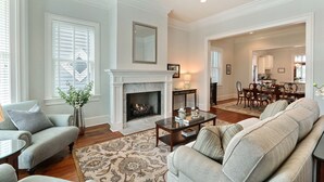 A spacious living room with a fireplace, a dining area, and a kitchen visible through an open doorway. - Heated Pool Access | 5*Clean | Flex Cancelation (Savannah)