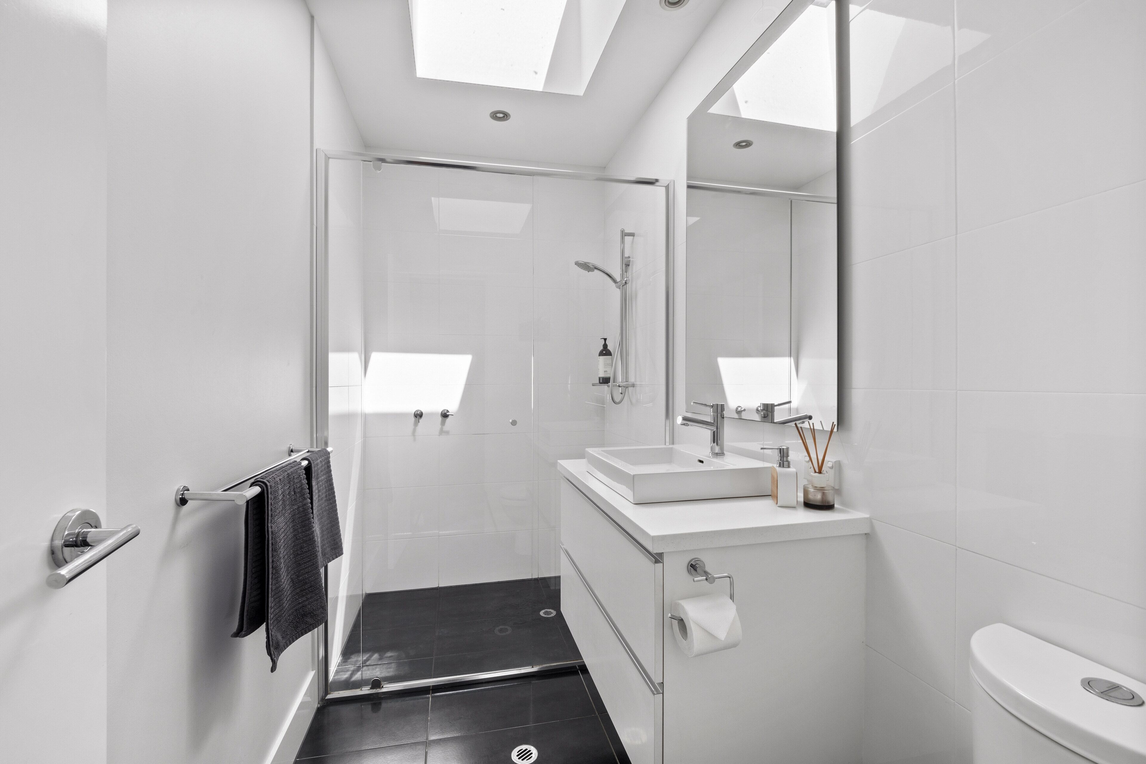Un baño moderno con cabina de ducha de vidrio, lavamanos blanco y un inodoro.